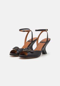 Black leather open-toe slingback heels with a buckle detail, brown insole, and a unique sculpted heel design. Smooth texture.