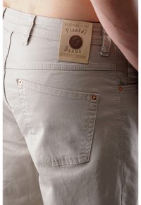 Hellgraue Denimjeans mit strukturierter Oberfläche, ausgestattet mit einem Markenpatch, kupfernen Nieten und einem Design der Gesäßtasche.