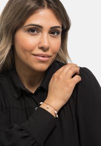 Bracciale con catena in oro rosa e molteplici accentuazioni di perle bianche. La modella indossa una blusa nera con colletto, mettendo in risalto i gioielli.