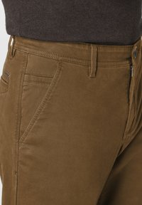 Braune Baumwollmischungshose mit glatter Textur, seitlichen Taschen, Reißverschluss und einem kontrastierenden Stichdetail an der Taille.