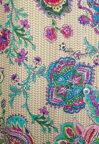 Barevná květinová látka s složitými vzory v růžové, modré a zelené na béžovém pozadí, s malým detailním knoflíkem.