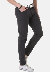 Slim-fit dunkelgraue Jeans mit einem strukturierten Muster, ausgestattet mit einer Vordertasche, metallenen Details und Seitennaht, kombiniert mit weißen Sneakers.
