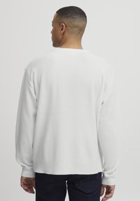 Chemise blanche à manches longues avec un design texturé en maille gaufrée. Dotée d'un col rond et de coutures d'épaule légèrement abaissées. Coupe décontractée.