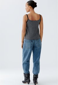 Grauer ärmelloser Top mit schwarzen Trägern, kombiniert mit locker sitzenden blauen Jeans und kniehohen schwarzen Stiefeln, von hinten gesehen.
