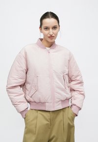 Giacca bomber rosa chiaro con zip frontale, colletto e polsini a coste, due tasche frontali e dettagli ricamati discreti. Tessuto liscio.