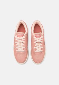 Różowe zamszowe sneakersy z perforowanym przodem, kremowymi sznurówkami i wyściełanym kołnierzem. Posiadają logo Reebok na języku oraz kolorowe akcenty po bokach.