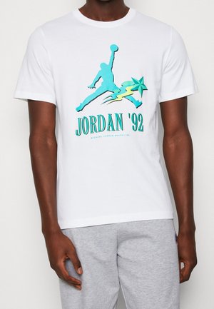Witte katoenen t-shirt met een grafische print van een springende figuur en een ster, met turquoise en gele accenten; ronde halslijn, korte mouwen.