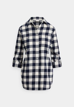 Pledēta pogājama krekls tumši zilā un krēmkrāsā, izgatavots no mīksta auduma. Tam ir apkakle, divas krūšu kabatas un uzpīts piedurkņu gals.