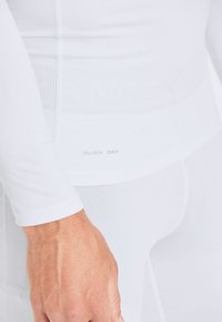 Wit, aansluitend sportshirt met lange mouwen, met een subtiele textuur en de tekst "QUICK DRY" aan de zoom. Glad en rekbaar materiaal.