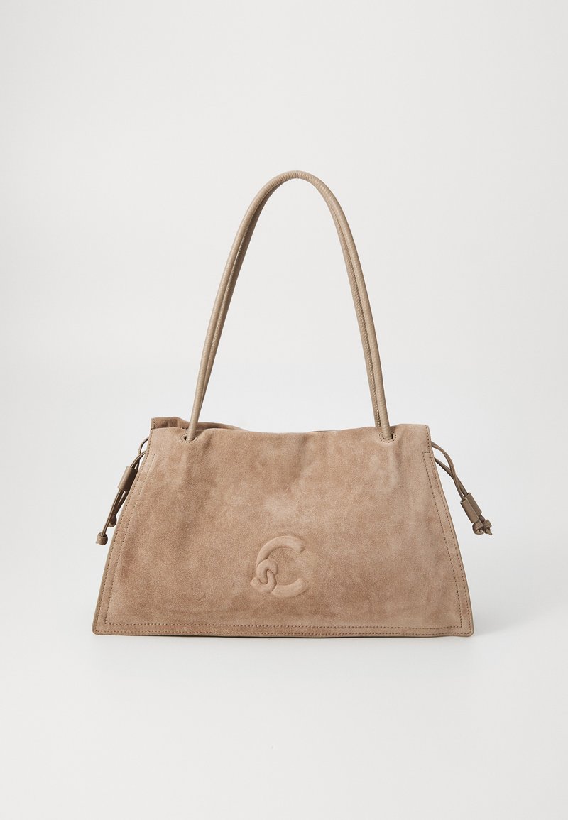 Bežna suede torba s strukturirano obliko, ki se ponaša z diskretnim logotipom vrezanim v material, dvema dolgima ročajema in okrasnimi vezmi ob straneh.