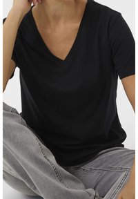 Svart kortärmad V-ringad t-shirt i mjukt material, med avslappnad passform och slät yta, kombinerad med ljusgrå denimjeans.