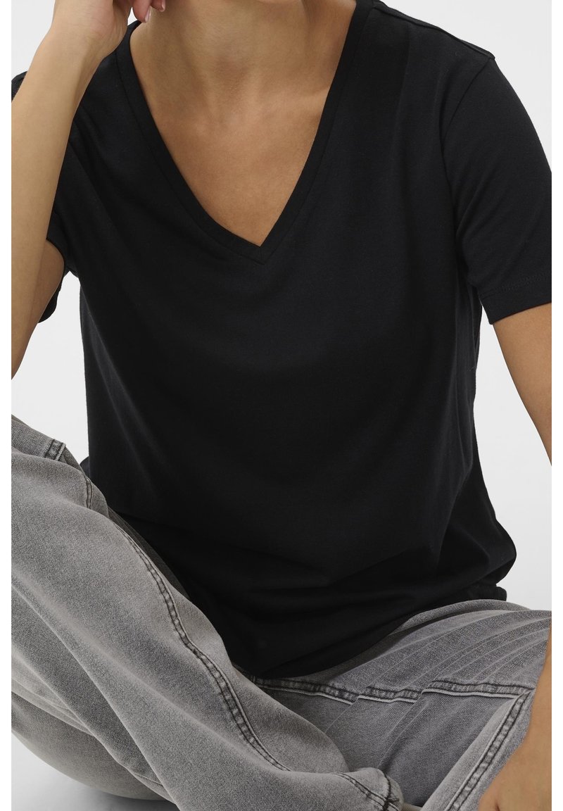 Svart kortärmad V-ringad t-shirt i mjukt material, med avslappnad passform och slät yta, kombinerad med ljusgrå denimjeans.