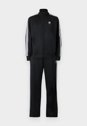 Tuta nera con giacca con zip e pantaloni. Realizzata in tessuto morbido, presenta strisce verticali bianche sulle maniche e sui lati, logo sul petto.