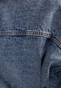 Denim fabric in light blue with a faded texture. Features orange stitching along seams and a smooth, soft drape.