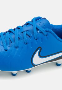 Modrá futbalová kopačka so syntetickým zvrškom, polstrovaným jazykom, textúrovaným povrchom, bielym logom Nike a tvarovanými kolíkmi pre trakciu.