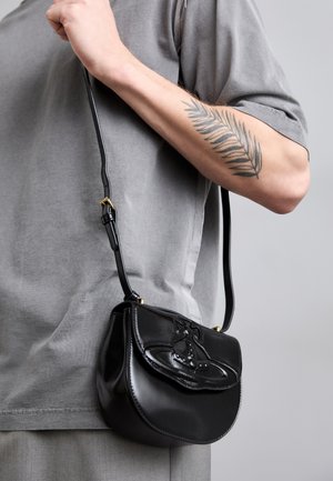 Black leather handbag with a curved shape, featuring a decorative design on the front, a short strap, and gold-tone hardware accents.