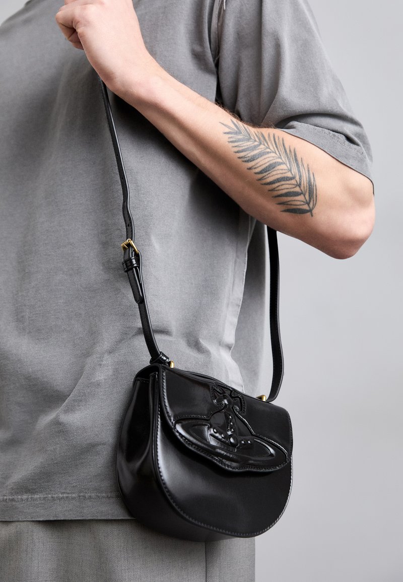 Black leather handbag with a curved shape, featuring a decorative design on the front, a short strap, and gold-tone hardware accents.