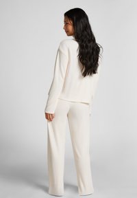 Licht crèmekleurig geribd loungewear-set met een relaxte fit, bestaande uit een langemouwen top en wijde broek. Zachte textuur met minimale stikseldetails.