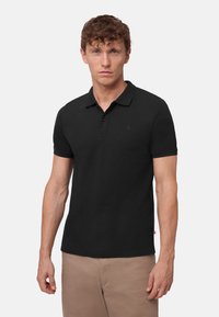 Zwarte poloshirt met korte mouwen, een kraag en een placket met twee knopen. Heeft een subtiele logo op de borst en een gestructureerde stof.