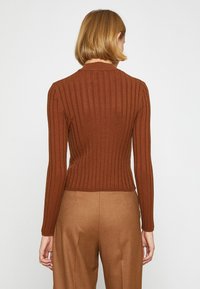 Brązowy sweter ze żebrowanym wzorem o dopasowanym kroju, z długimi rękawami i wysokim dekoltem, w połączeniu z beżowymi spodniami o wysokim stanie. Miękka faktura.