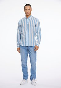 Camisa de botones a rayas en azul claro y beige, con cuello y mangas largas. Combinada con jeans azul claro y zapatillas blancas.