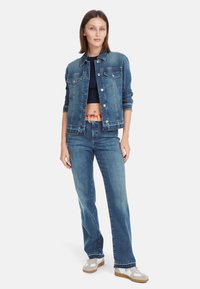 Denim jacket in light blue with a cropped design, two chest pockets, and silver buttons. Paired with straight-leg jeans and beige sneakers.