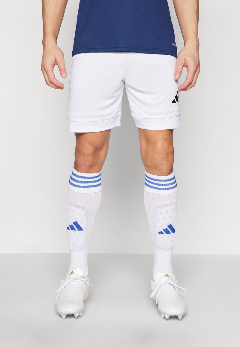Shorts de sport blancs avec des accents bleus, associés à des chaussettes blanches rayées de bleu et des chaussures blanches avec des détails dorés. Détails : Adidas.