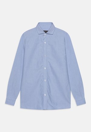 Chemise bleu clair à manches longues avec col pointu, soigneusement étalée à plat sur un fond blanc.