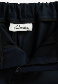 Navy blue, gathered waist ja zip pocket olev kangas, millel on valge silt, kus on kirjas "Clarks". Sile tekstuur ilma nähtavate mustriteta.