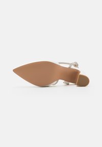 Hvit stiletthæl med spiss tå, gjennomsiktig rem, og en tan gummisåle. Silkeaktig tekstur med minimal detaljering.