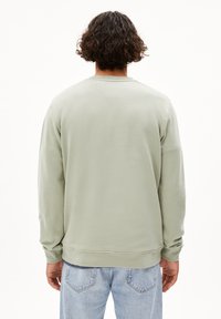 Hellgrüner Sweatshirt mit langen Ärmeln, Rundhalsausschnitt und gerippten Bündchen. Weicher Stoff; getragen mit hellblauen Jeans.