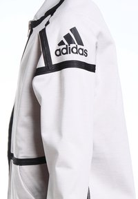 Weißes Adidas-Jackett mit schwarzen horizontalen Streifen, seitlichem Reißverschluss und Adidas-Logo am oberen Arm.