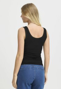 Canottiera nera con un design aderente, scollatura rotonda e spalline sottili; tessuto testurizzato si raccoglie leggermente in vita, indossata con jeans blu.