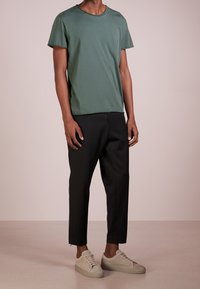 Grön bomullströja med korta ärmar, ihopparad med svarta avsmalnande byxor. Outfiten fullbordas med ljusgrå sneakers med subtil textur.