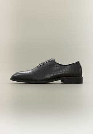 Chaussure habillée pour homme en cuir noir avec texture crocodile, design à lacets et talon bas, vue de profil sur fond neutre.