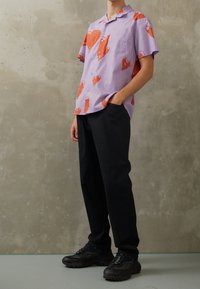 Košile s krátkým rukávem v levandulové barvě s vzory červených srdcí; spárována s černými kalhotami a masivními černými teniskami; hladká tkanina, volný střih.