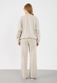 Lichtbeige loungewear-set met een losse sweatshirt met een brede manchet en bijpassende wijde broek, gemaakt van zachte, gestructureerde stof.