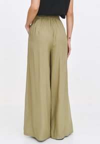 Oliwkowe, szerokie spodnie z elastycznym paskiem w talii. Wykonane z gładkiego materiału, z dwoma bocznymi kieszeniami oraz luźnym krojem.
