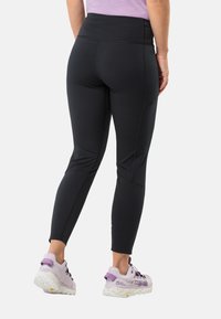 Zwarte sportleggings met een hoge tailleband, voorzien van platte naden en een aansluitende pasvorm. Gecombineerd met lichtpaarse trailschoenen.