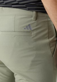 Ανοιχτό πράσινο αθλητικό παντελόνι με πίσω τσεπούλα και γκρι λογότυπο Adidas. Το ύφασμα φαίνεται λείο με ελαφριά ελαστικότητα.