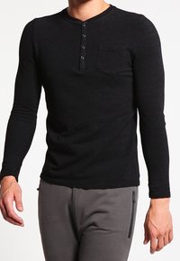 Camisa henley negra de manga larga con cuello redondo, tapeta con tres botones y bolsillo en el pecho. Tejido suave y con textura.