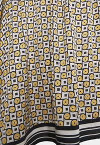 Udbredt nederdel fremstillet af vævet stof, der har et gentaget mønster af gule blomster på en hvid baggrund med sorte firkanter og striber.