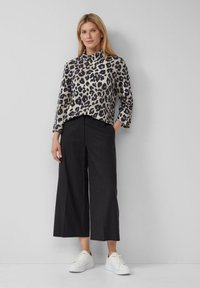 Maglione a collo alto con stampa leopardata in beige e nero, abbinato a pantaloni neri a gamba larga con vita alta e sneakers bianche. Sfondo semplice.