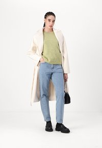 Kremfarget ullfrakk, lys grønn genser, blå jeans og svarte loafers. Tilbehøret inkluderer en liten svart håndveske med kjede.