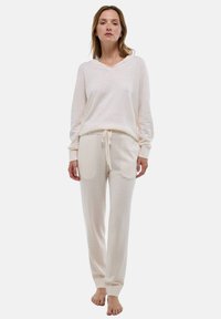 Ensemble de loungewear de couleur crème clair comprenant un haut à capuche à manches longues et un pantalon à cordon avec des poignets côtelés ; les deux sont fabriqués en tissu doux et texturé.