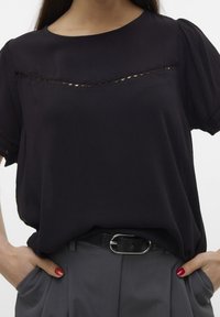Blouse noire à manches courtes avec un col rond, présentant un détail de découpe horizontal sur la poitrine et un tissu doux et léger.