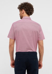 Kurzarm, kariertes Hemd in Pink mit klassischem Kragen, glatter Textur und geradem Saum, kombiniert mit dunkelblauen Hosen.