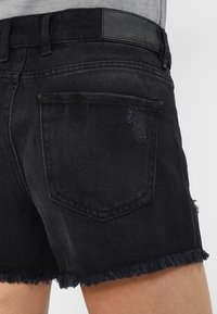 Mustat farkkushortsit, joissa on risat helmat, kahdella takataskulla ja vyötäröllä oleva nahkaleima, jossa lukee "NOISY MAY".