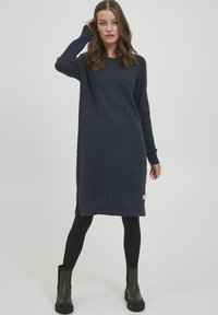 Marinblå stickad klänning med långa ärmar, sidospaltar och avslappnad passform, kombinerad med svarta leggings och klackade ankelstövlar.