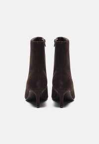 Brune semskede ankelstøvletter med en avtagende silhuett, høye stiletthæler og glidelåser bak. Myk tekstur med en jevn finish.
